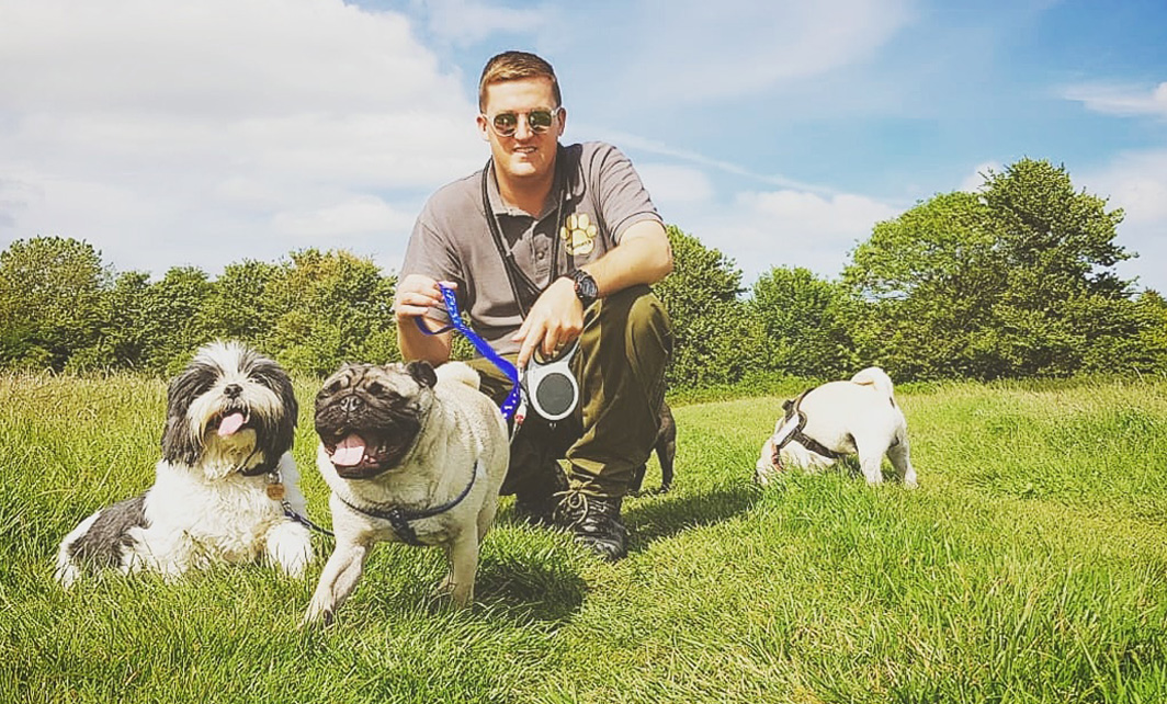 Leon Gray kneeling with 2 pugs and a shitzu in sunny field