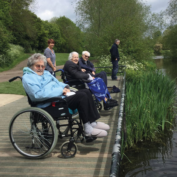Three elderly residents of Pembroke House in wheelchairs looking over pond