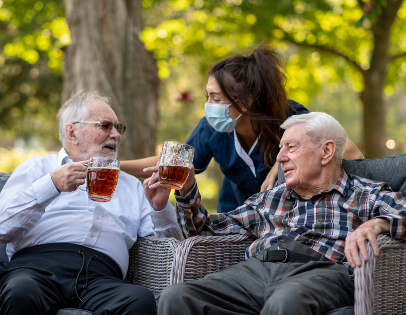 Two Pembroke House residents enjoying a pint of beer with staff member conversing while wearing mask