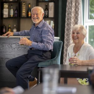 Two residents in entertainment area of Admiral Jellicoe House smiling with drinks in hand